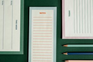 Organized flatlay featuring notepads and colored pencils on a green background.