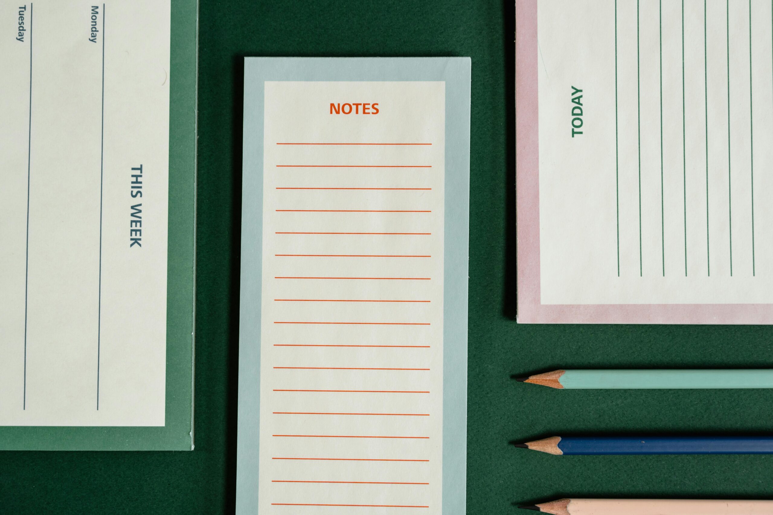 Organized flatlay featuring notepads and colored pencils on a green background.