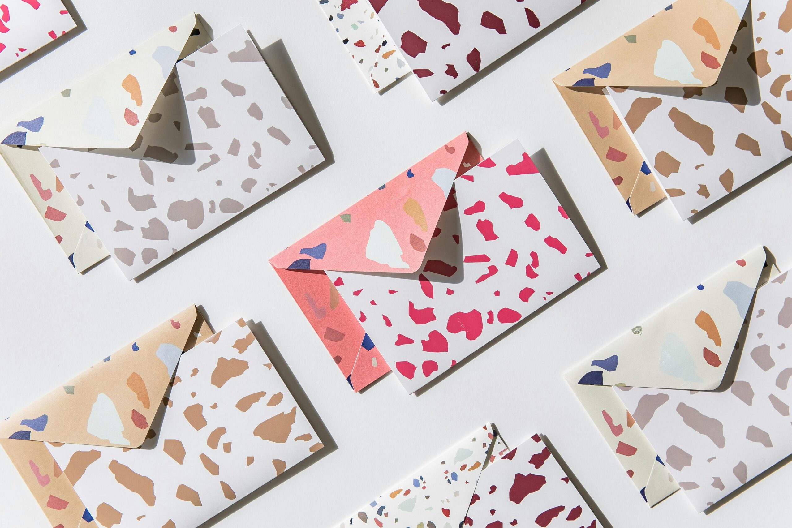 Artistic flat lay of vibrant patterned envelopes with terrazzo design on white surface.